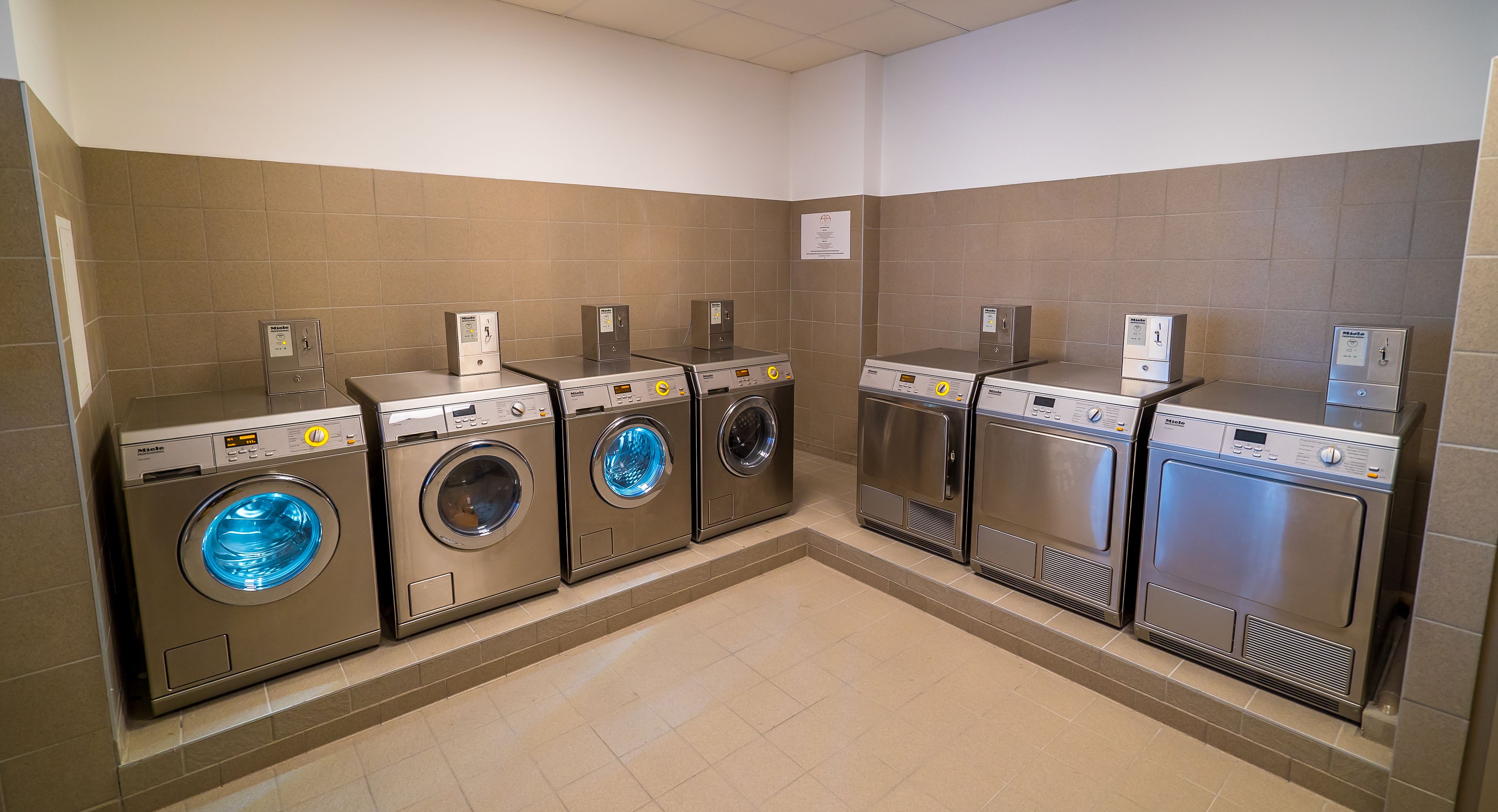 Une laverie équipée de six lave-linge et six sèche-linge à chargement frontal, disposés en deux rangées.