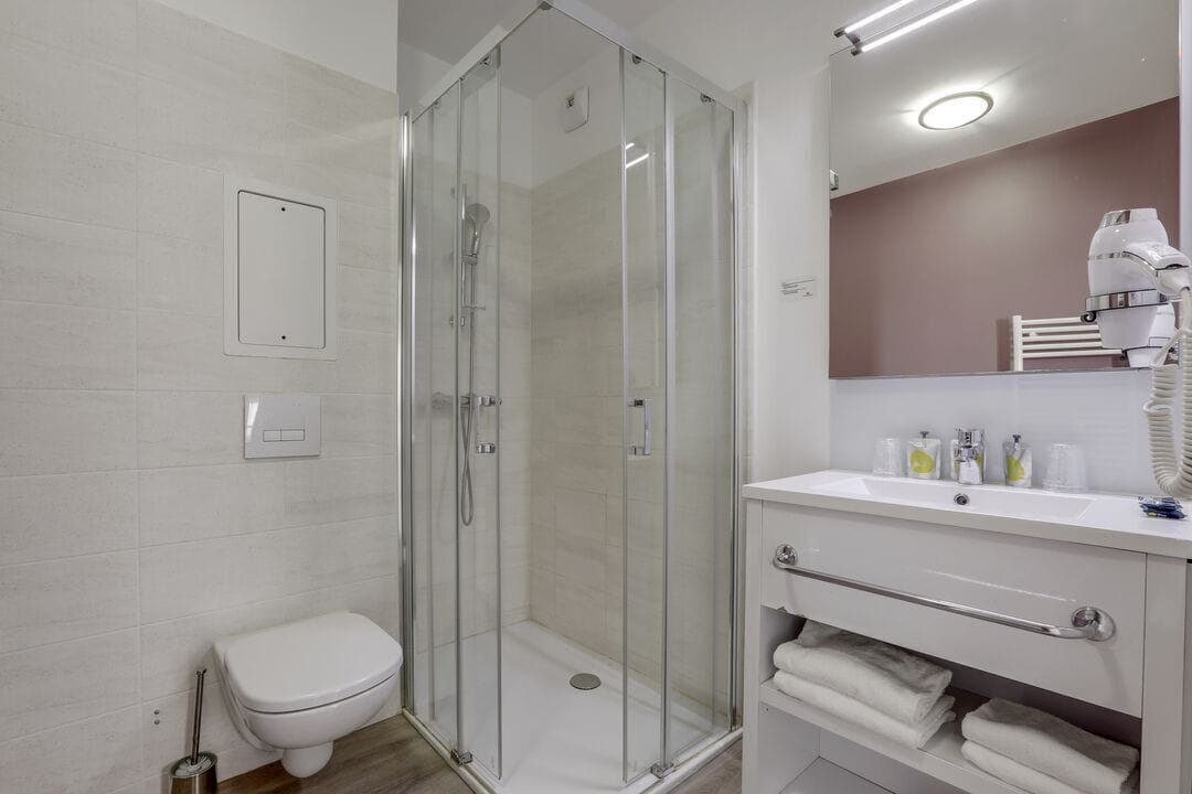 Un baño moderno con ducha de vidrio, inodoro blanco y tocador con espejo y toallero.