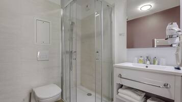 Un baño moderno con ducha de vidrio, inodoro blanco y tocador con espejo y toallero.