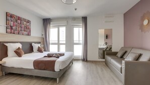 A modern hotel room with a large bed, a sofa, a bathroom, and a view of the city.