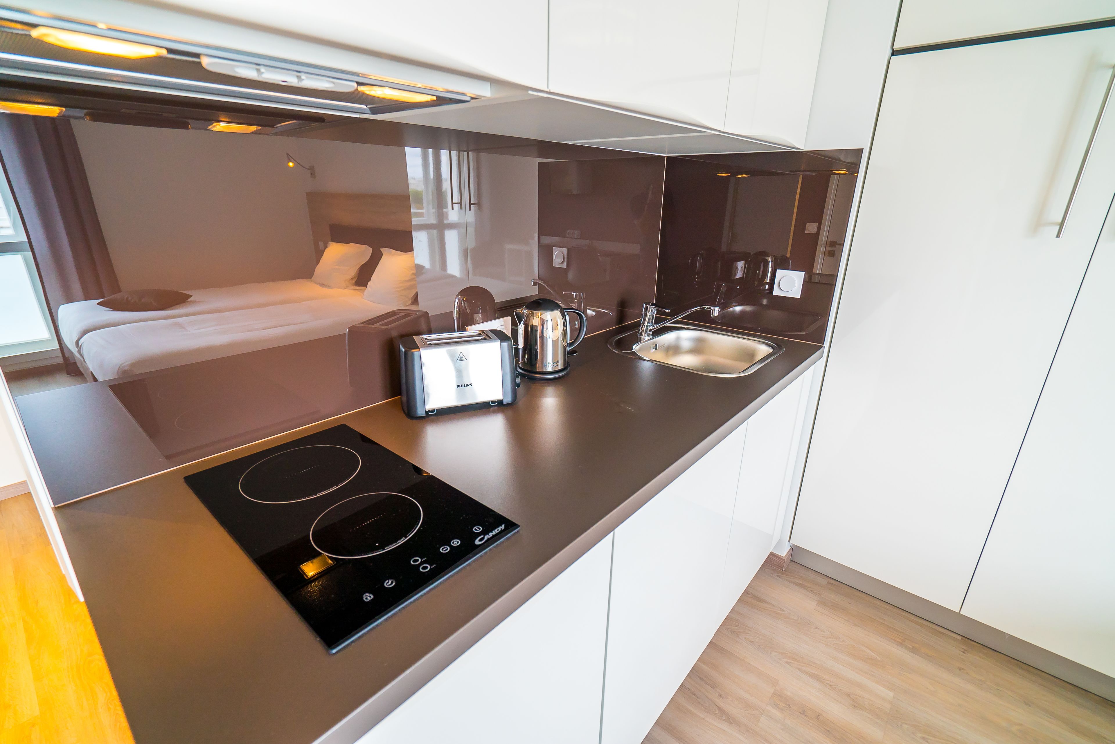 Een compact keukenhoekje met een ingebouwde kookplaat, broodrooster en waterkoker, naast een bed met uitzicht op de omgeving.