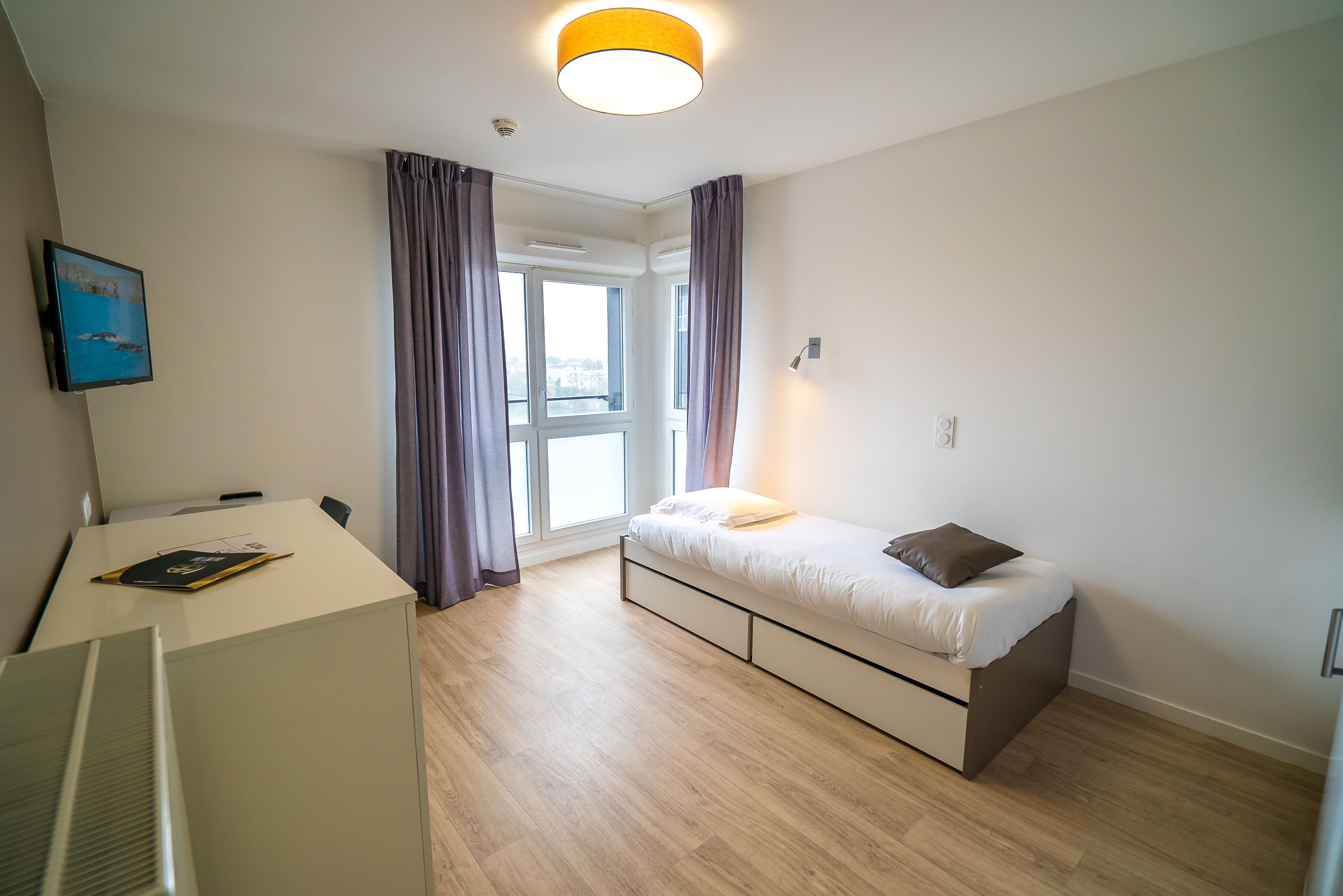 A modern bedroom with a bed, a desk, and a window with curtains.