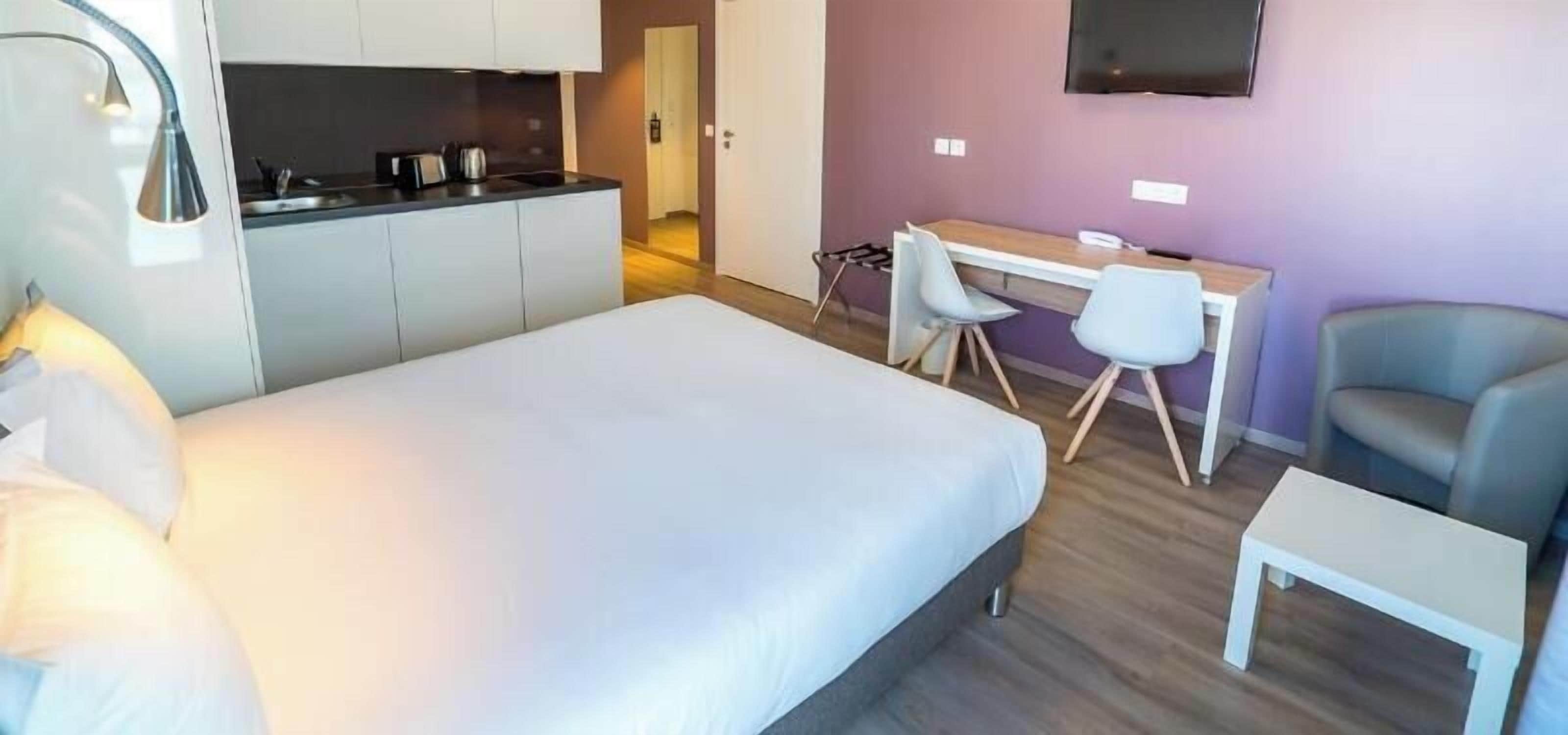 Een hotelkamer met een bed, een bureau, twee stoelen, een televisie en een klein tafeltje.