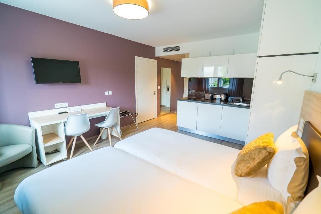 Una habitación de hotel moderna con una cama, un escritorio, una silla, un televisor y una kitchenette.