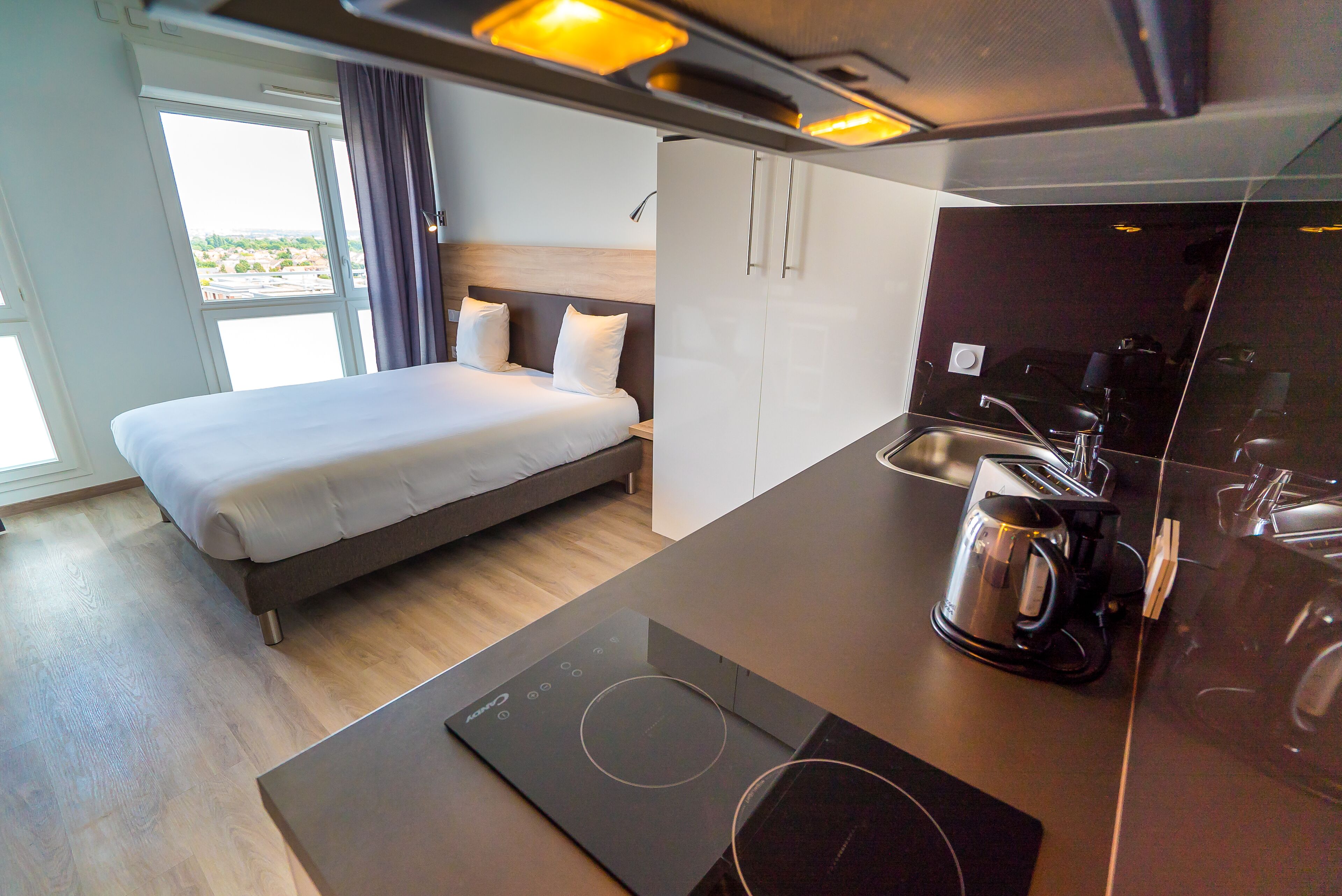 Une chambre d’hôtel moderne avec un lit, une petite kitchenette et une vue sur la ville.