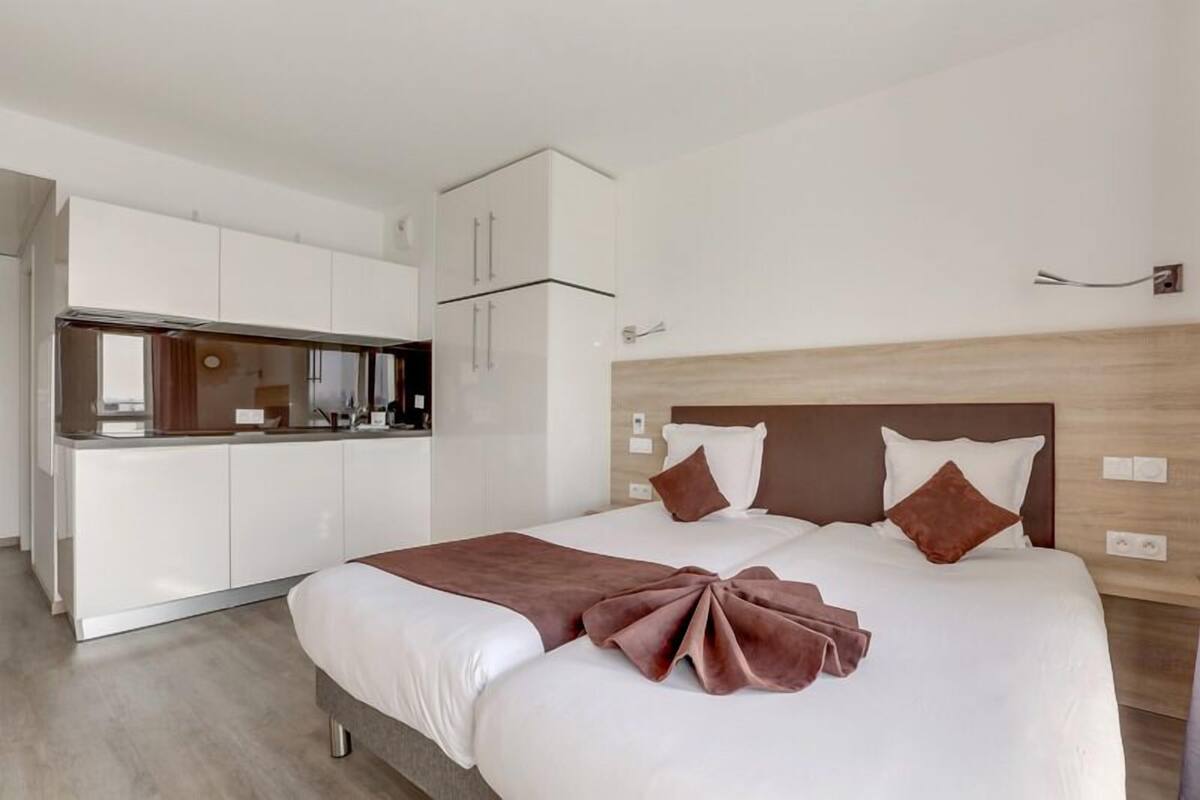 Une chambre d’hôtel moderne équipée d’un lit, d’une kitchenette et d’une tête de lit en bois.