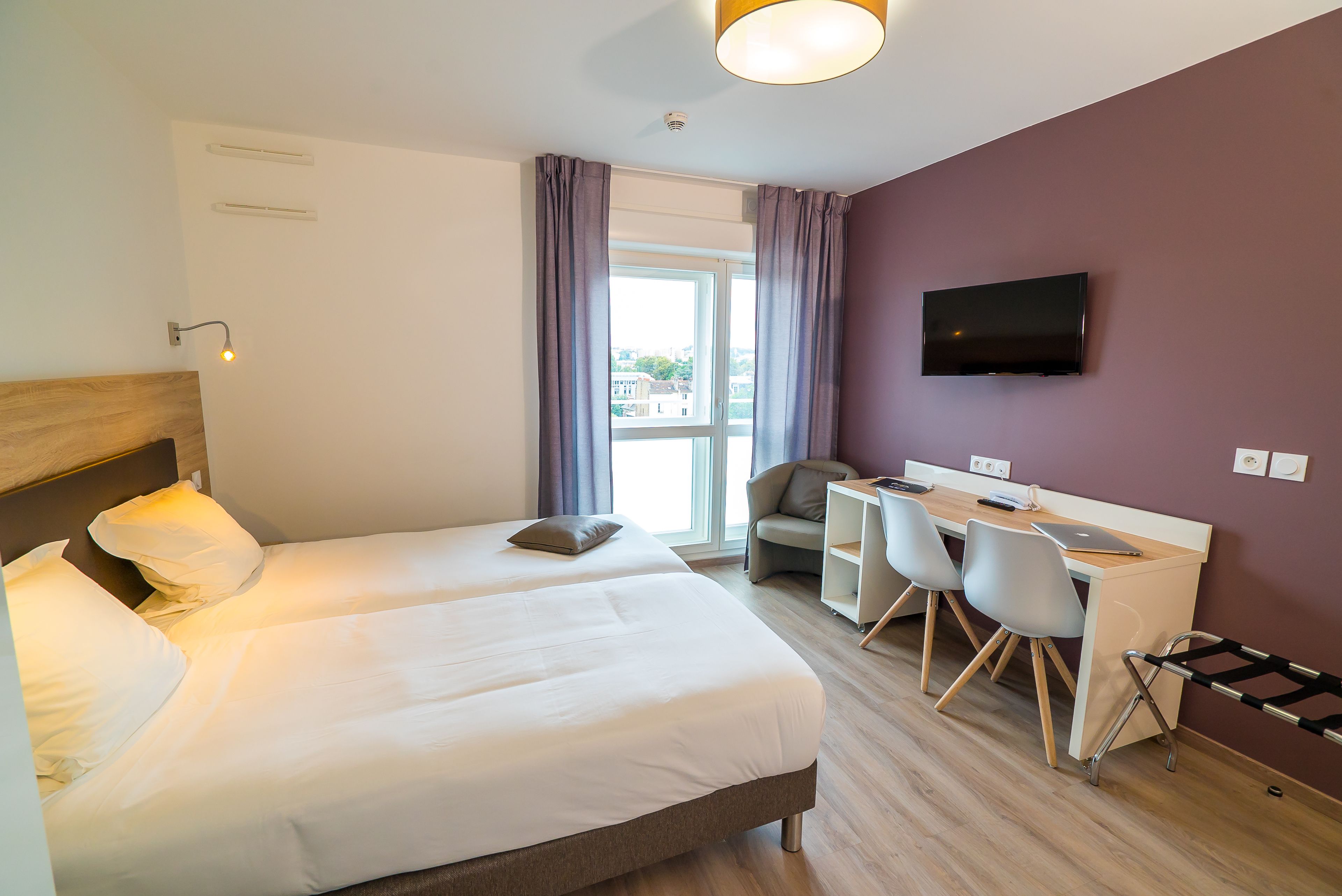 A hotel room with two beds, a desk, a chair, a TV, and a window with curtains.