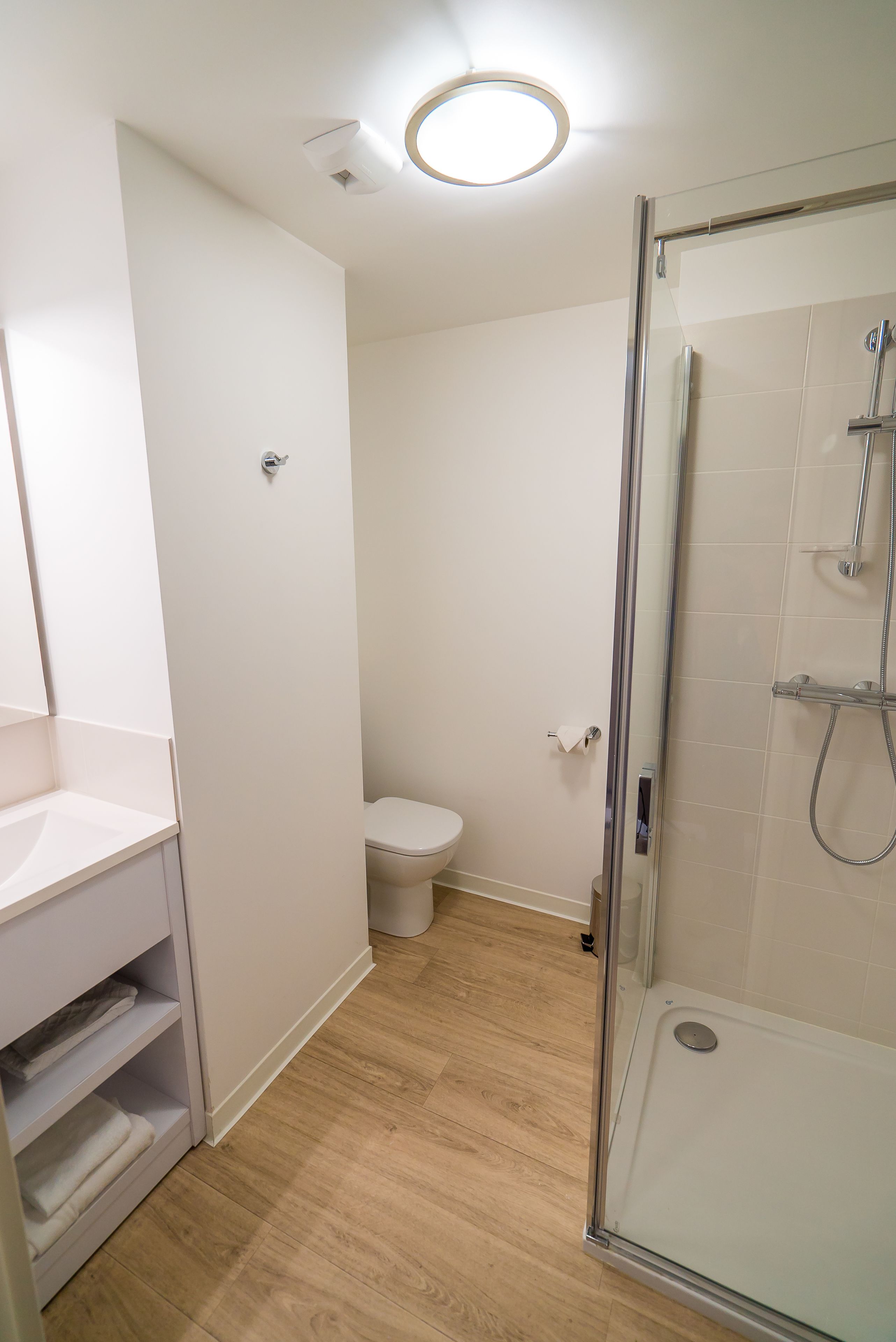 A bathroom with a glass shower enclosure, a toilet, and a white sink with a mirror.