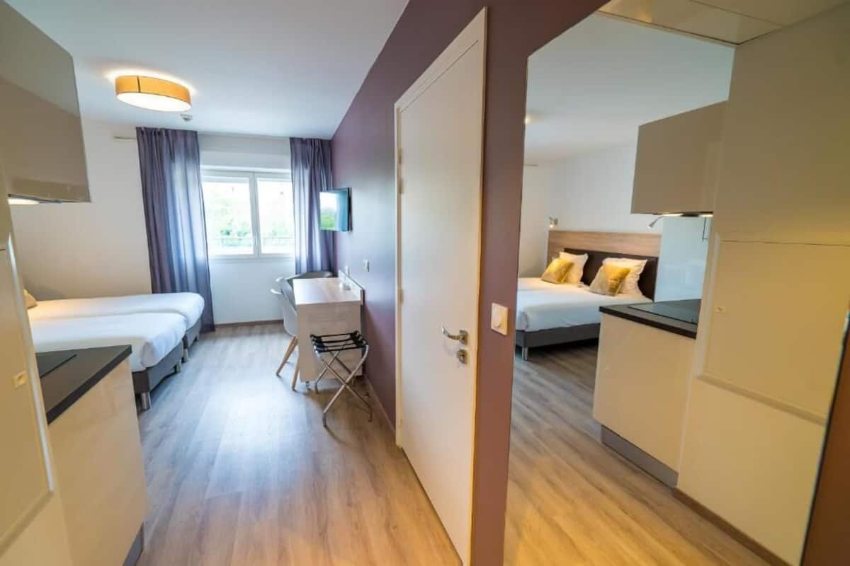 Une chambre d’hôtel avec deux lits, un bureau, une chaise et une télévision.