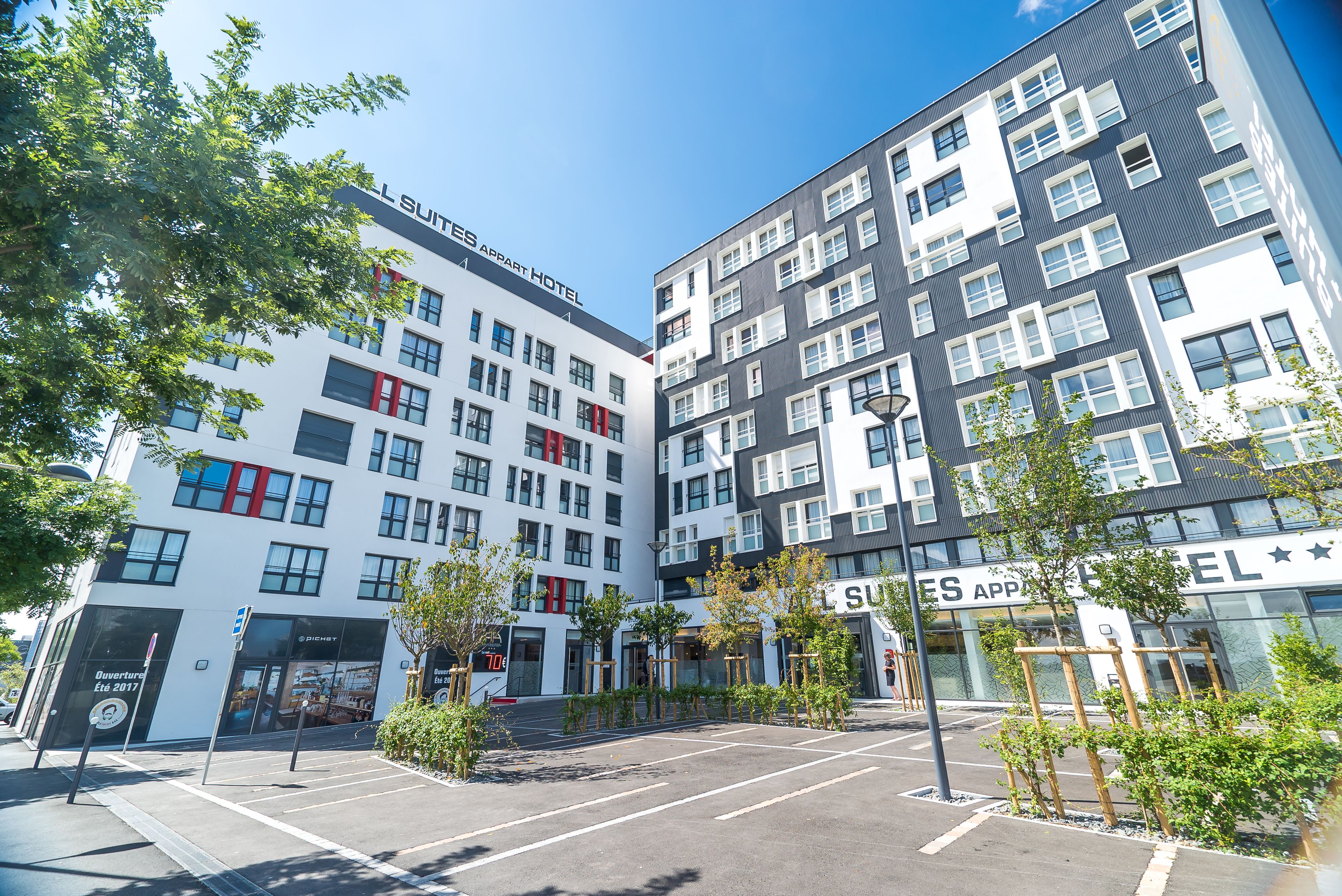 A modern hotel with multiple floors, large windows, and a parking area with trees.
