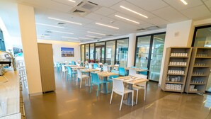 A modern cafeteria with tables and chairs, a vending machine, and a glass door leading outside.