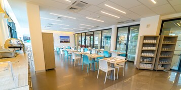 Una cafetería moderna con mesas y sillas, una máquina expendedora y una puerta de vidrio que da al exterior.