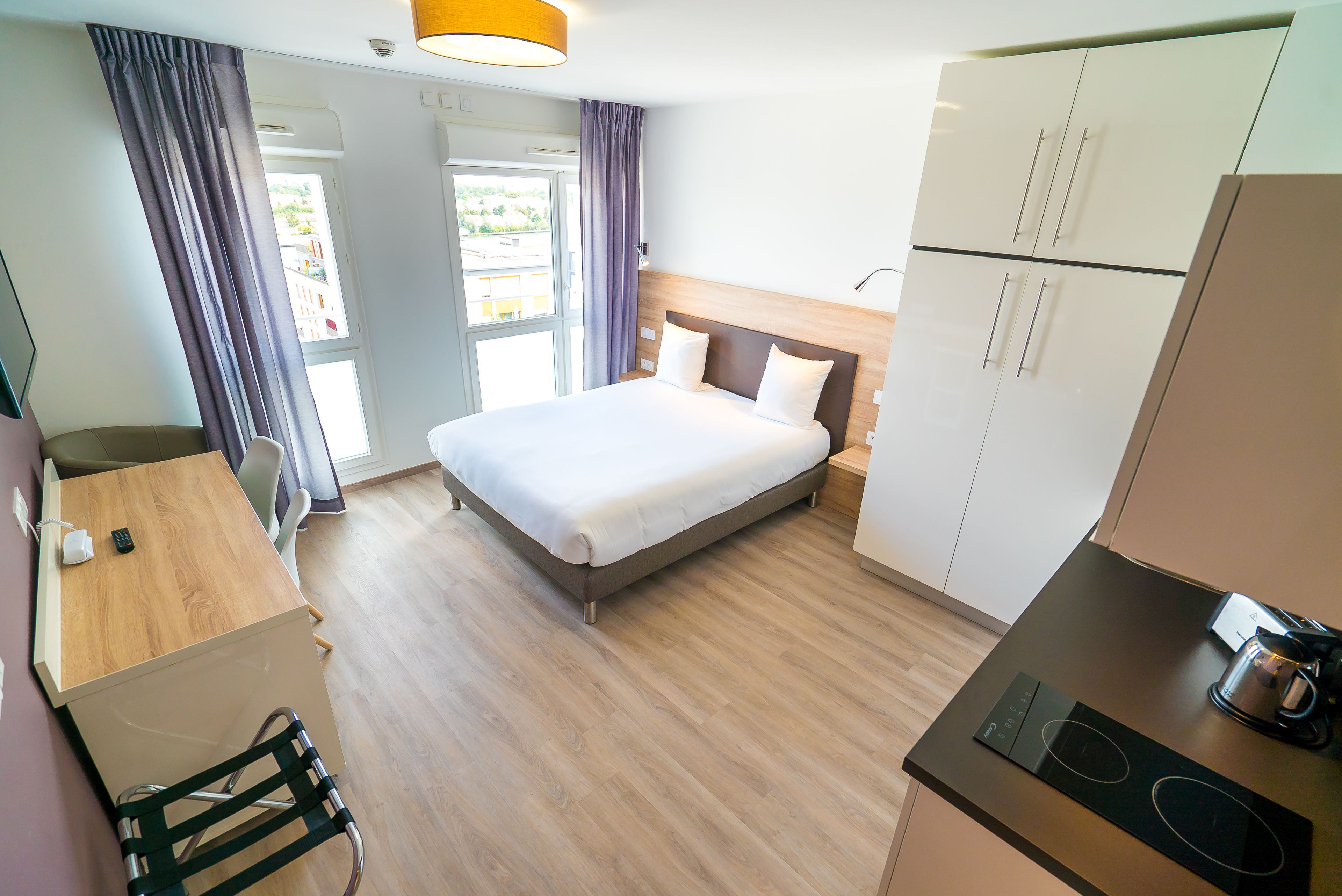Een moderne hotelkamer met een bed, bureau, stoel, kitchenette en uitzicht op het landschap.