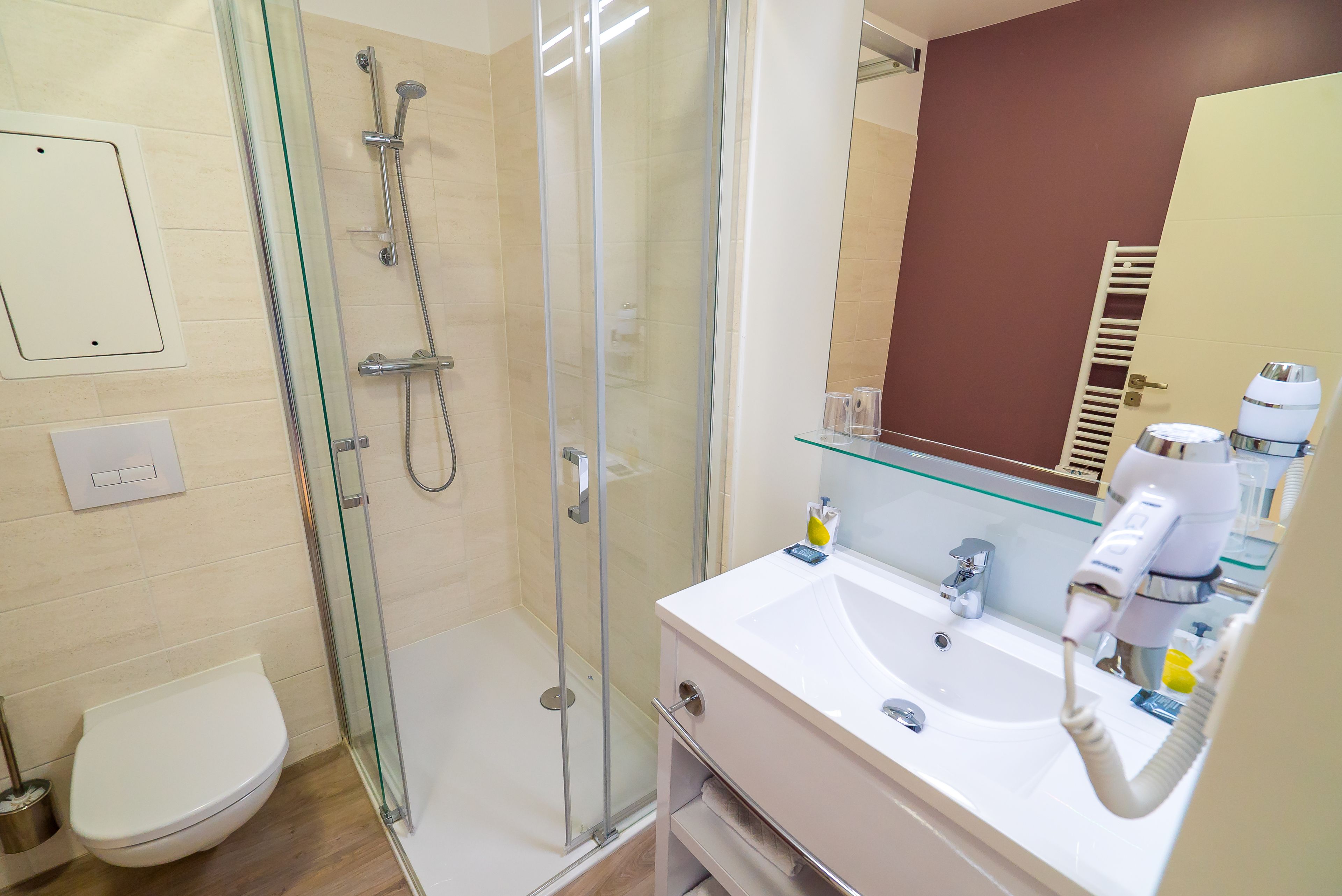 Een moderne badkamer met een douche met glazen wand, een wit wastafelmeubel met een glazen plank en een spiegel boven het wastafelmeubel.