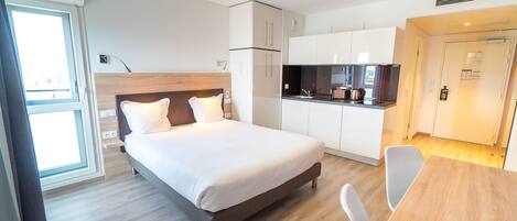 Una habitación de hotel moderna con una cama grande, kitchenette y comedor.