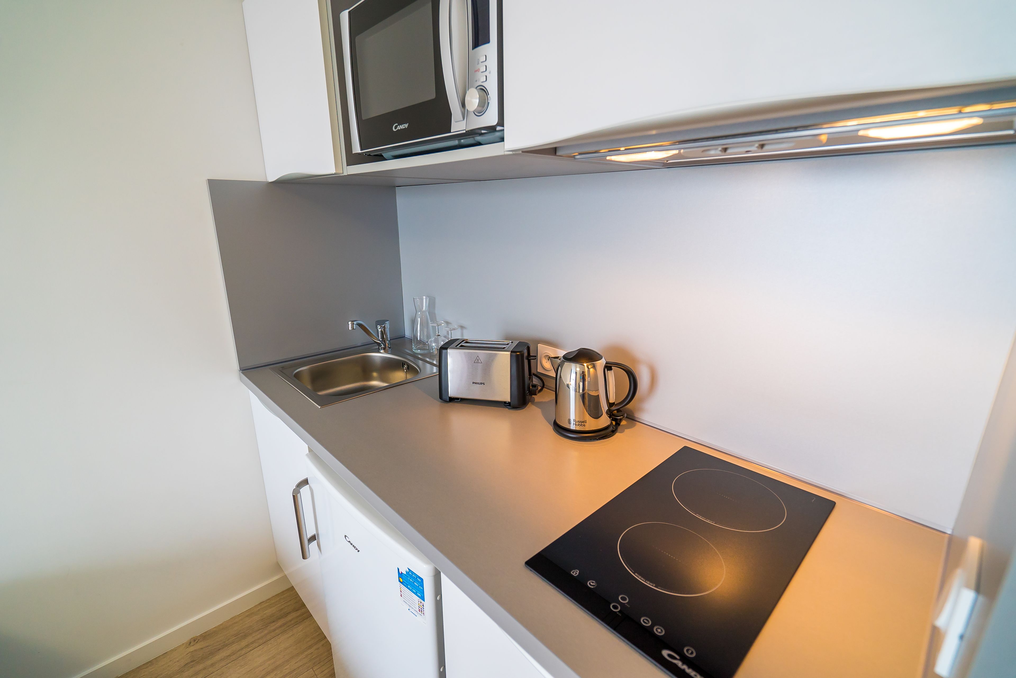 Una kitchenette compacta equipada con microondas, tostadora, hervidor y placa de inducción.