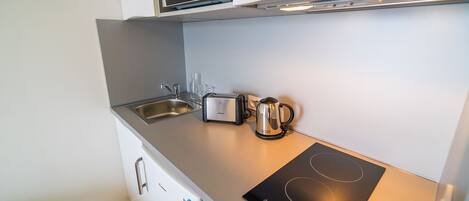 Una kitchenette compacta equipada con microondas, tostadora, hervidor y placa de inducción.