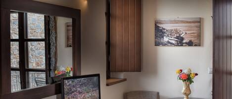 A room with a large window, a flat-screen TV, a small round table with a vase, a chair, and a wooden cabinet.
