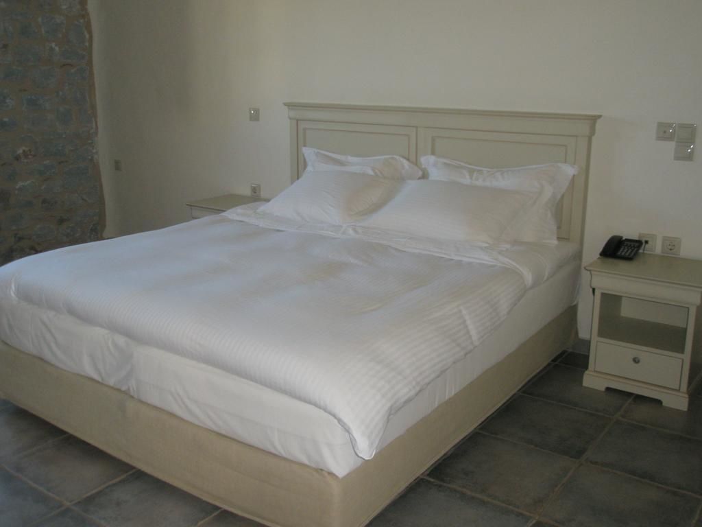 A neatly made bed with white bedding in a room with a stone wall and tiled floor.