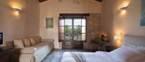 Un dormitorio con una cama grande, un sofá, una mesita de noche con una lámpara y vistas a través de una puerta.