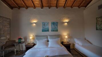 A bedroom with a large bed, two bedside tables, a chair, and a stone wall.