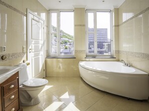 A bathroom with a toilet, a sink, and a bathtub. There are two windows providing views of buildings and greenery. - Prize by Radisson, Xhibition Bergen City (Bergen)
