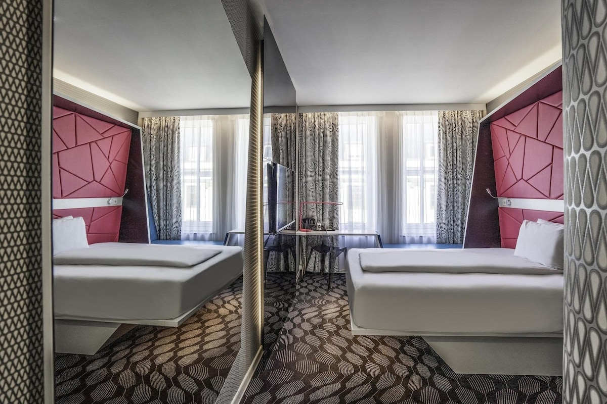 A hotel room with two beds, a desk, and a TV.
