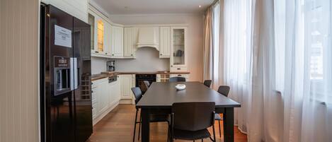 Une cuisine moderne avec des meubles blancs, un réfrigérateur noir et une table à manger avec des chaises.