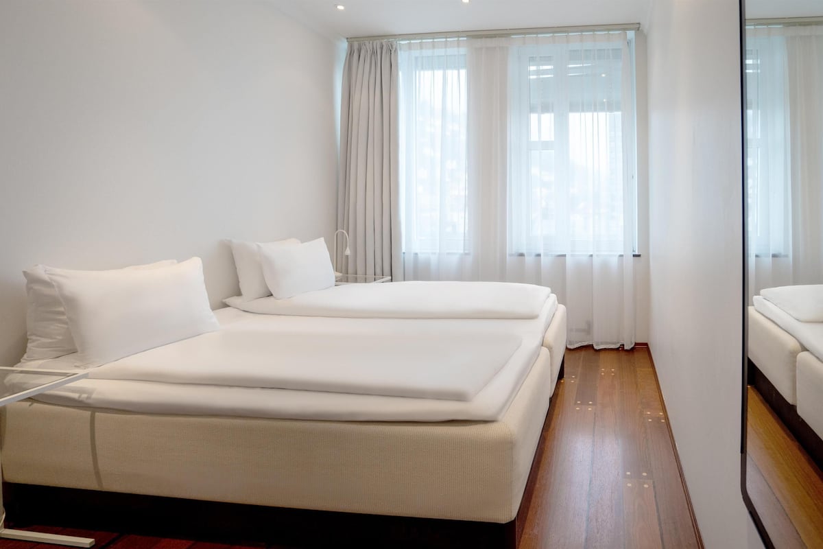 A hotel room with two beds, a wooden floor, and large windows with curtains.