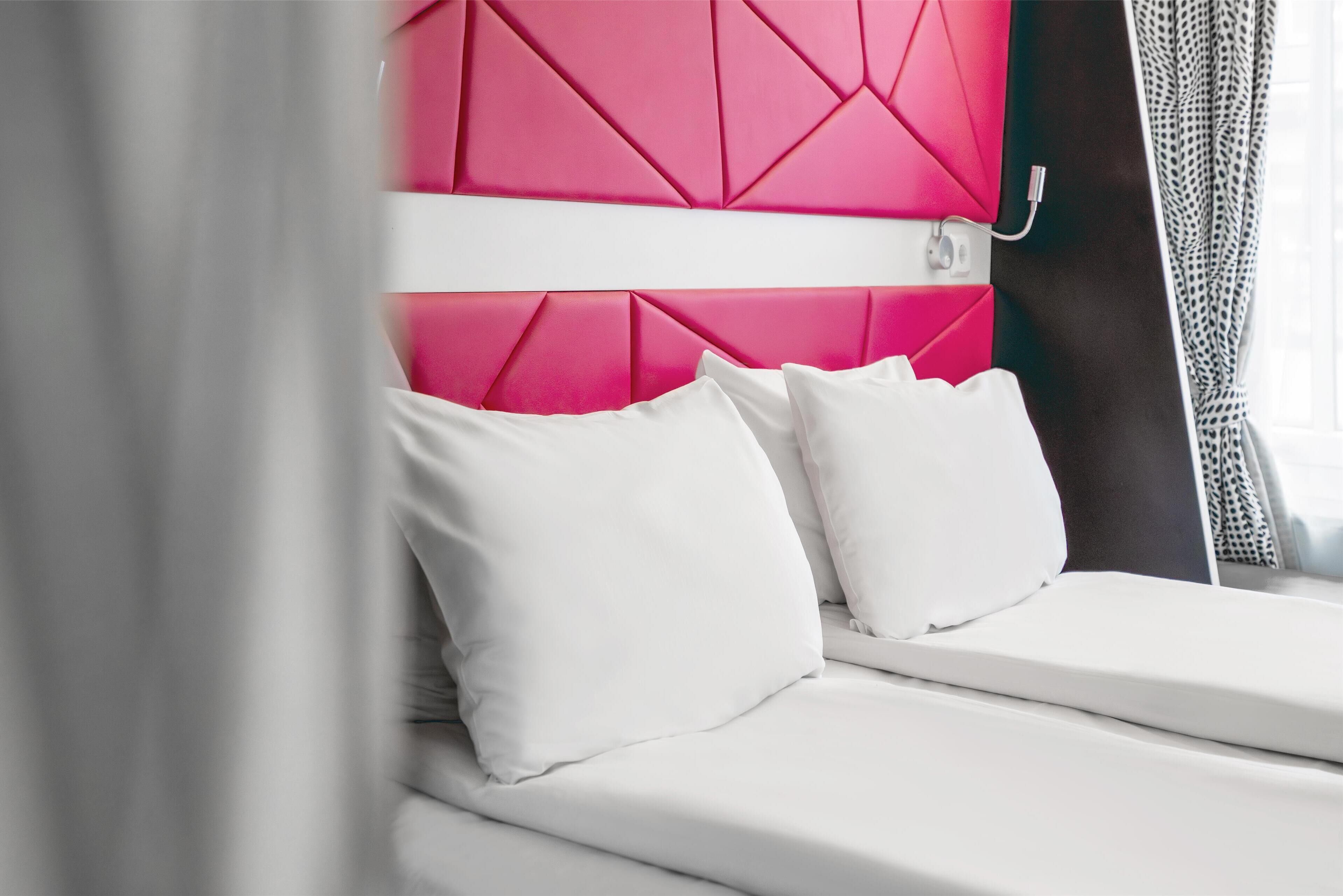 A bed with white bedding and a pink headboard.