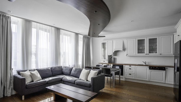 A modern living room with a sectional sofa, a wooden coffee table, and a kitchen area with white cabinets and a refrigerator. - Prize by Radisson, Xhibition Bergen City (Bergen)