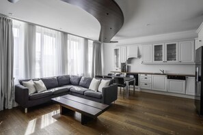 A modern living room with a sectional sofa, a wooden coffee table, and a kitchen area with white cabinets and a refrigerator. - Prize by Radisson, Xhibition Bergen City (Bergen)