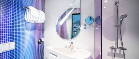 Un baño moderno con pared de azulejos azules, un espejo redondo, un lavabo blanco y una ducha con mampara de vidrio.