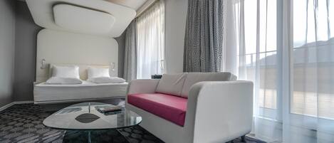 Une chambre d’hôtel moderne avec un canapé blanc, une table basse en verre et un tapis à motifs.