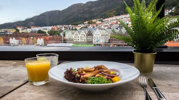 A table with a plate of food, a glass of orange juice, a potted fern, and cutlery.
