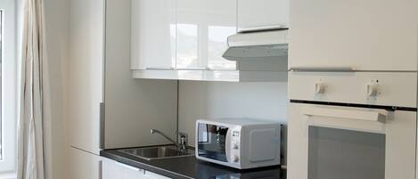 Una cucina moderna con mobili bianchi, un piano di lavoro nero ed elettrodomestici integrati, tra cui un forno a microonde e un forno.