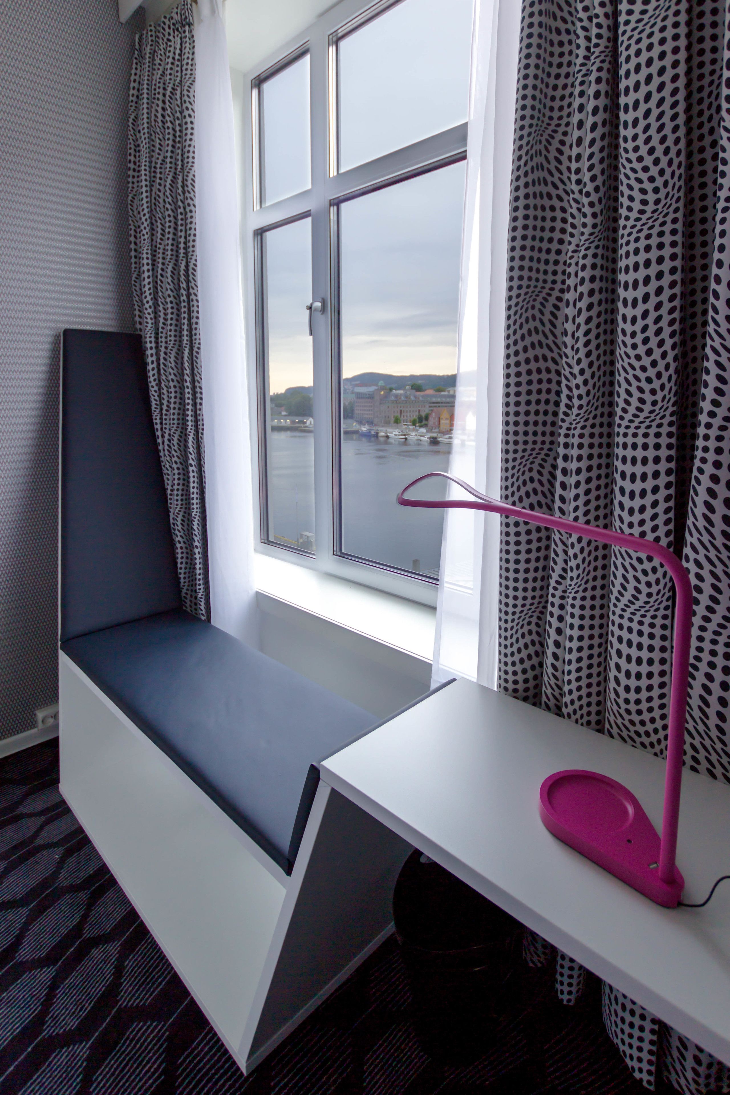 Una habitación con una ventana, un escritorio y una lámpara rosa.
