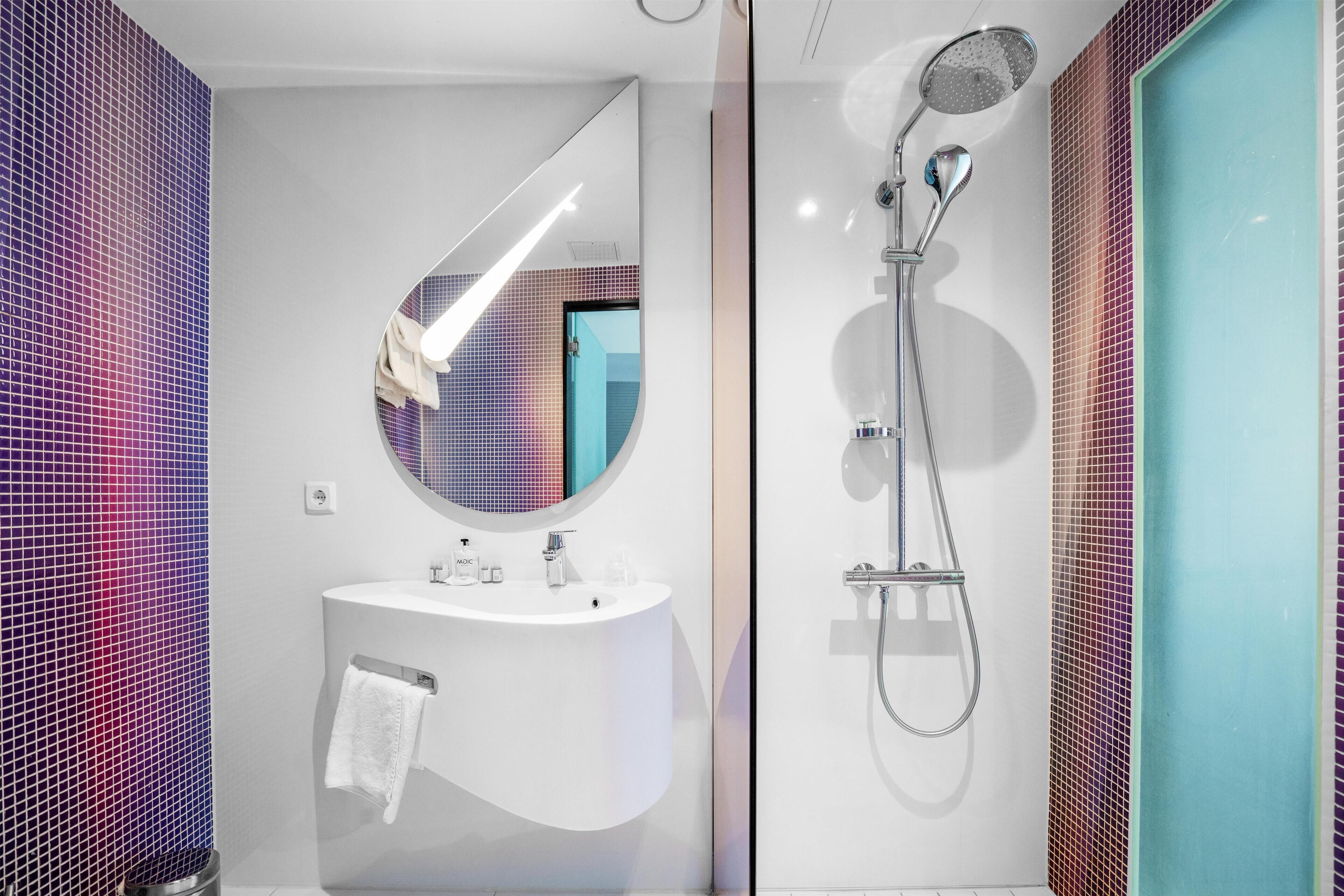 A modern bathroom with a white sink, a round mirror, and a shower with a handheld showerhead.