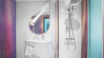 Une salle de bain moderne avec un lavabo blanc, un miroir rond et une douche équipée d’un pommeau de douche à main.