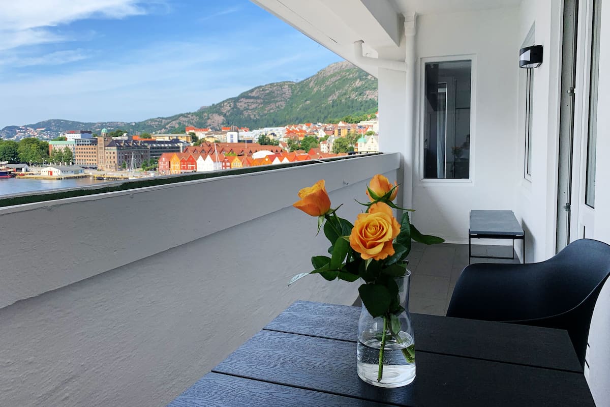 Un balcon avec une table, un vase rempli de roses et une vue sur le paysage urbain et les montagnes.