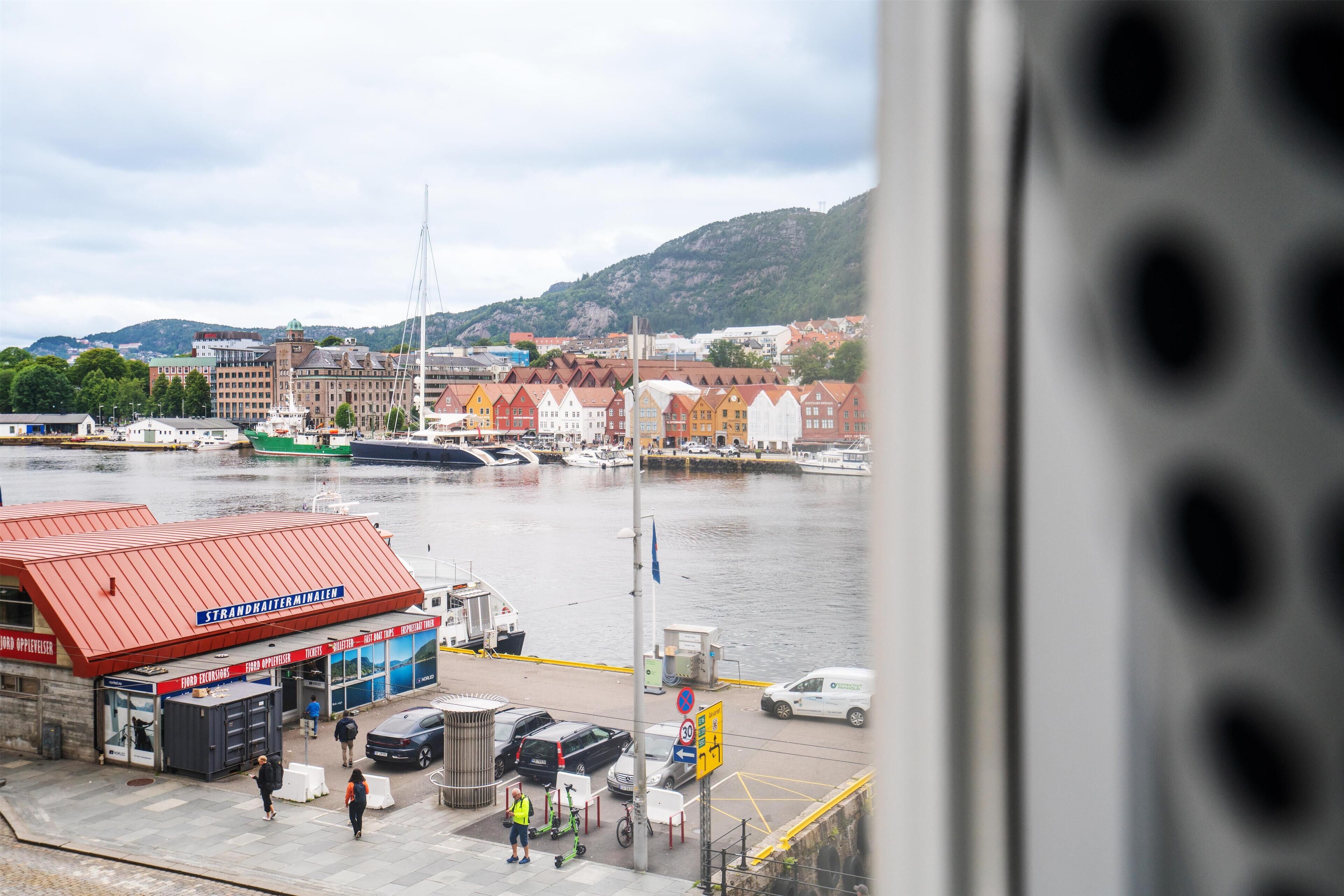 A harbor with boats, a red-roofed building labeled "Strandnahtemineralen," and a hilly landscape in the background.