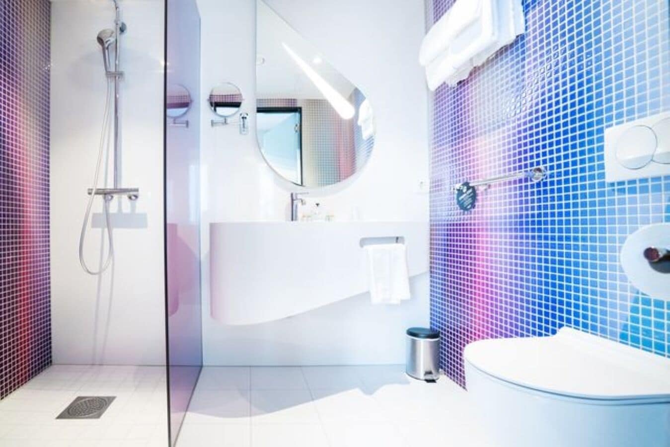 Un baño moderno con ducha de vidrio, lavamanos blanco y pared con azulejos azules.