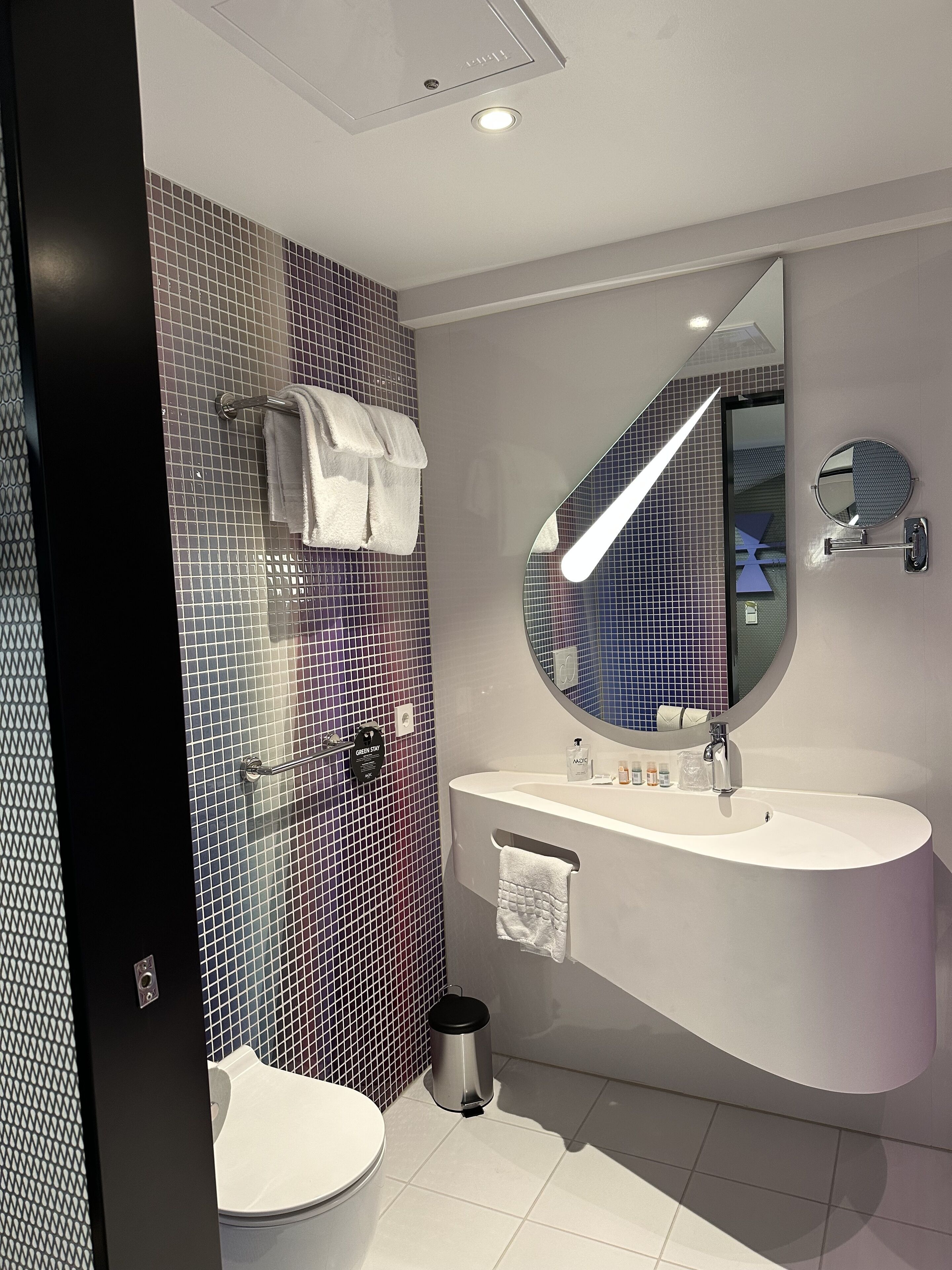 Une salle de bain moderne avec un lavabo blanc, un miroir rond et un mur recouvert de carreaux.