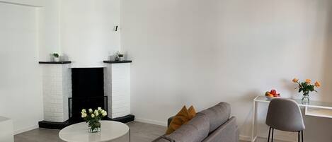 A modern living room with a fireplace, a grey sofa, a round coffee table, and a small white table with a vase of flowers.