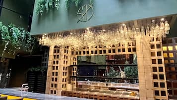 Zona de bar interior con diseño moderno, que incluye una barra, asientos y detalles decorativos como luces colgantes y plantas.