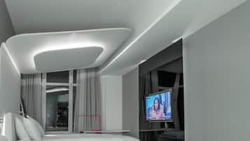 A modern living room with a glass coffee table, a white sofa with a pink cushion, and a flat-screen TV mounted on the wall.