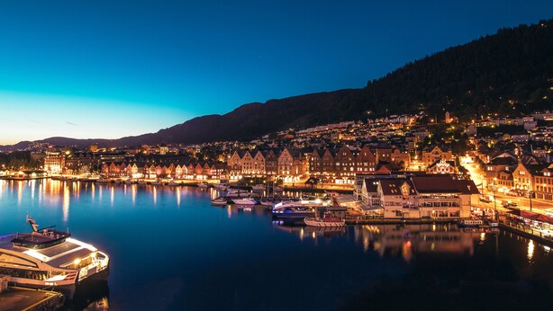 A waterfront town with historic buildings, a marina, and a hill in the background.