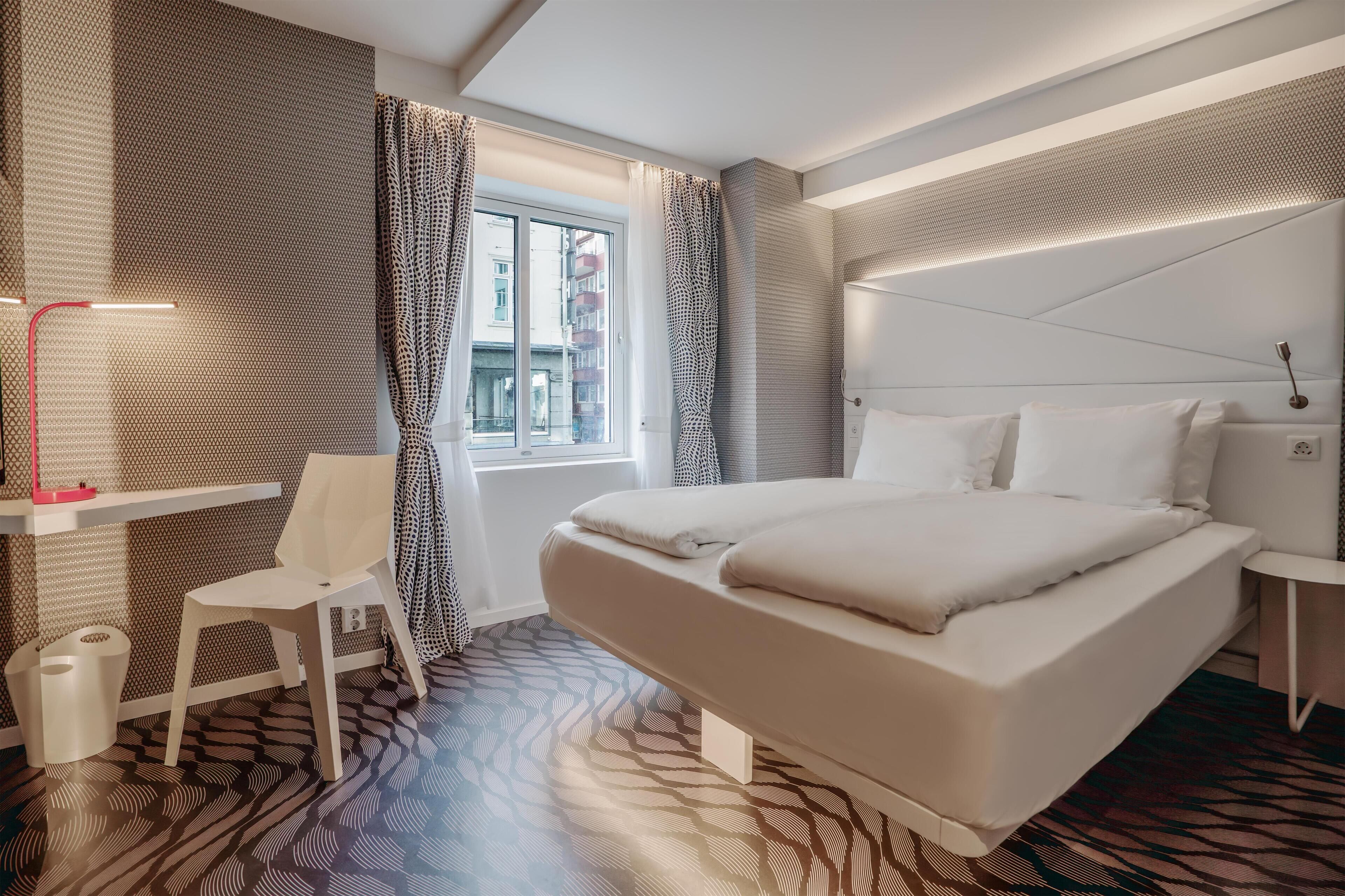 A modern hotel room with a large bed, a desk, and a chair.