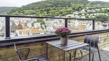A balcony with a wooden railing, a table, two chairs, and a potted plant with pink flowers.