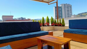 Une terrasse sur le toit, aménagée avec du mobilier en bois, dotée d’une verrière et offrant une vue sur le paysage urbain.